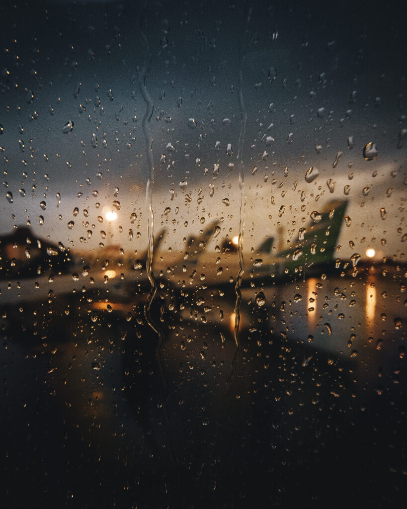 View of airplanes at dusk through a window splattered with rain drops